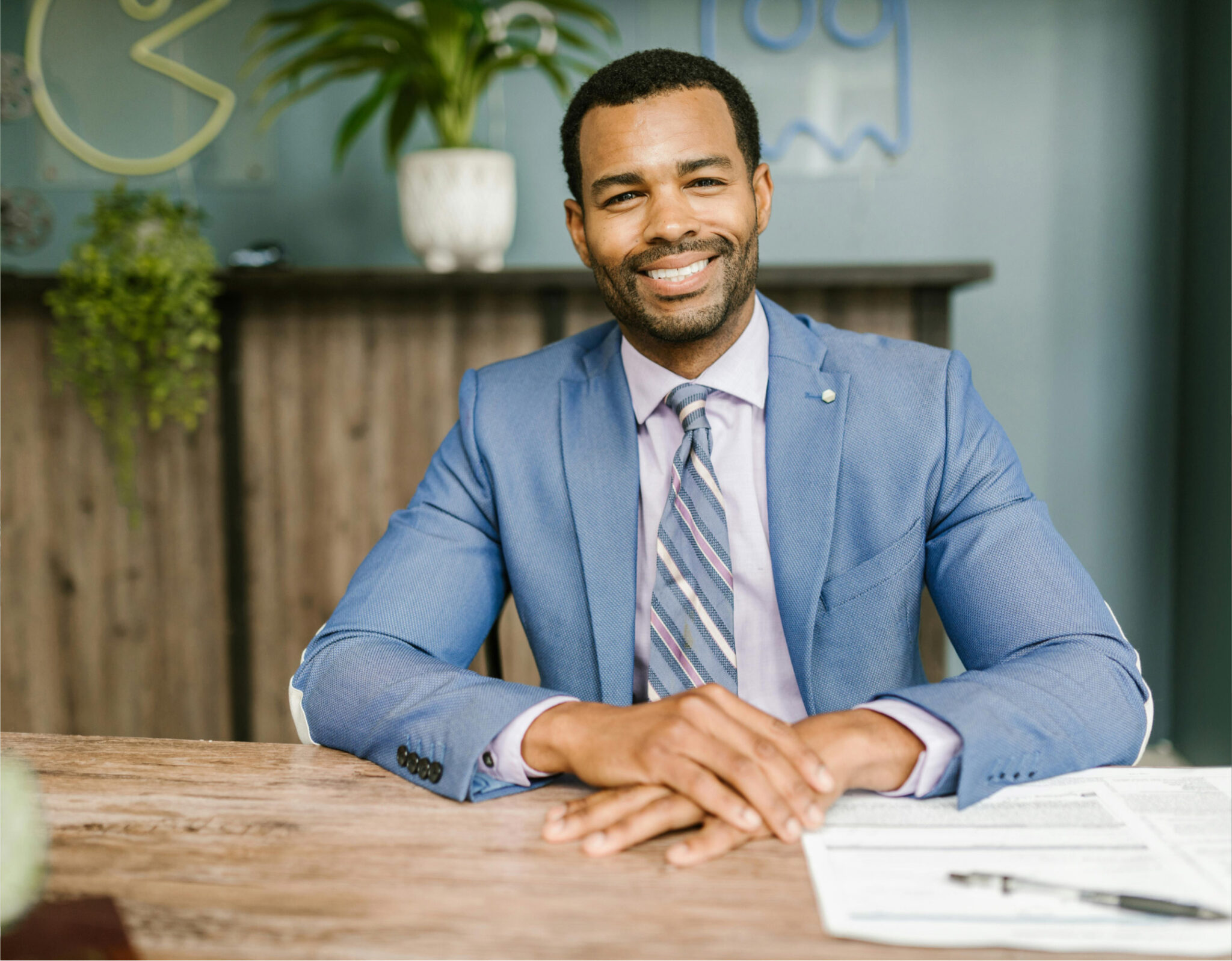 Man in blue suit smiling at desk.