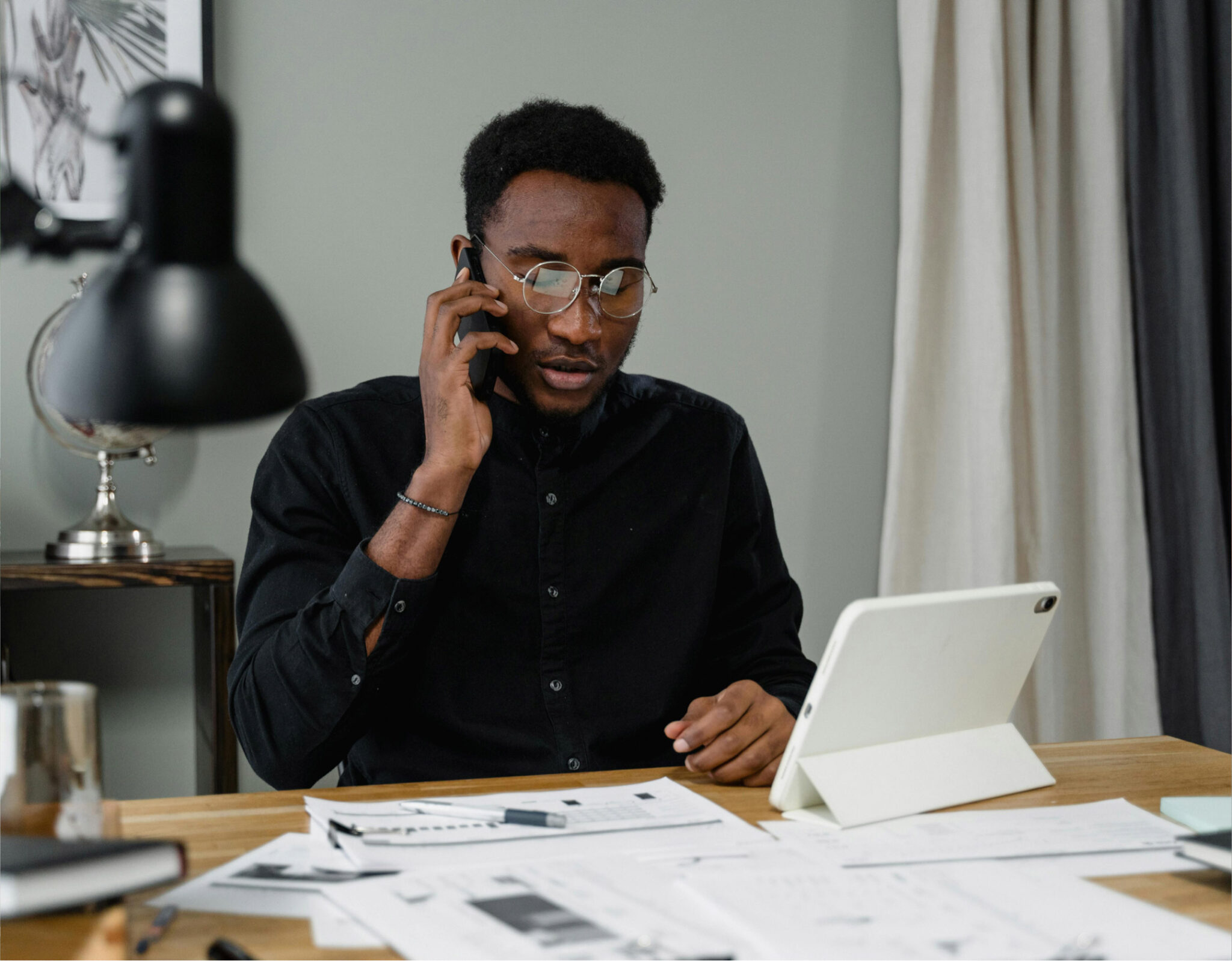 Man talking on phone, using tablet at desk.