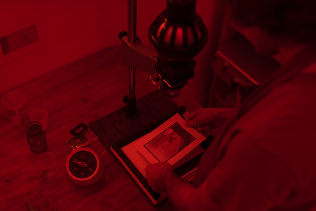 Person developing photo in darkroom with red light.