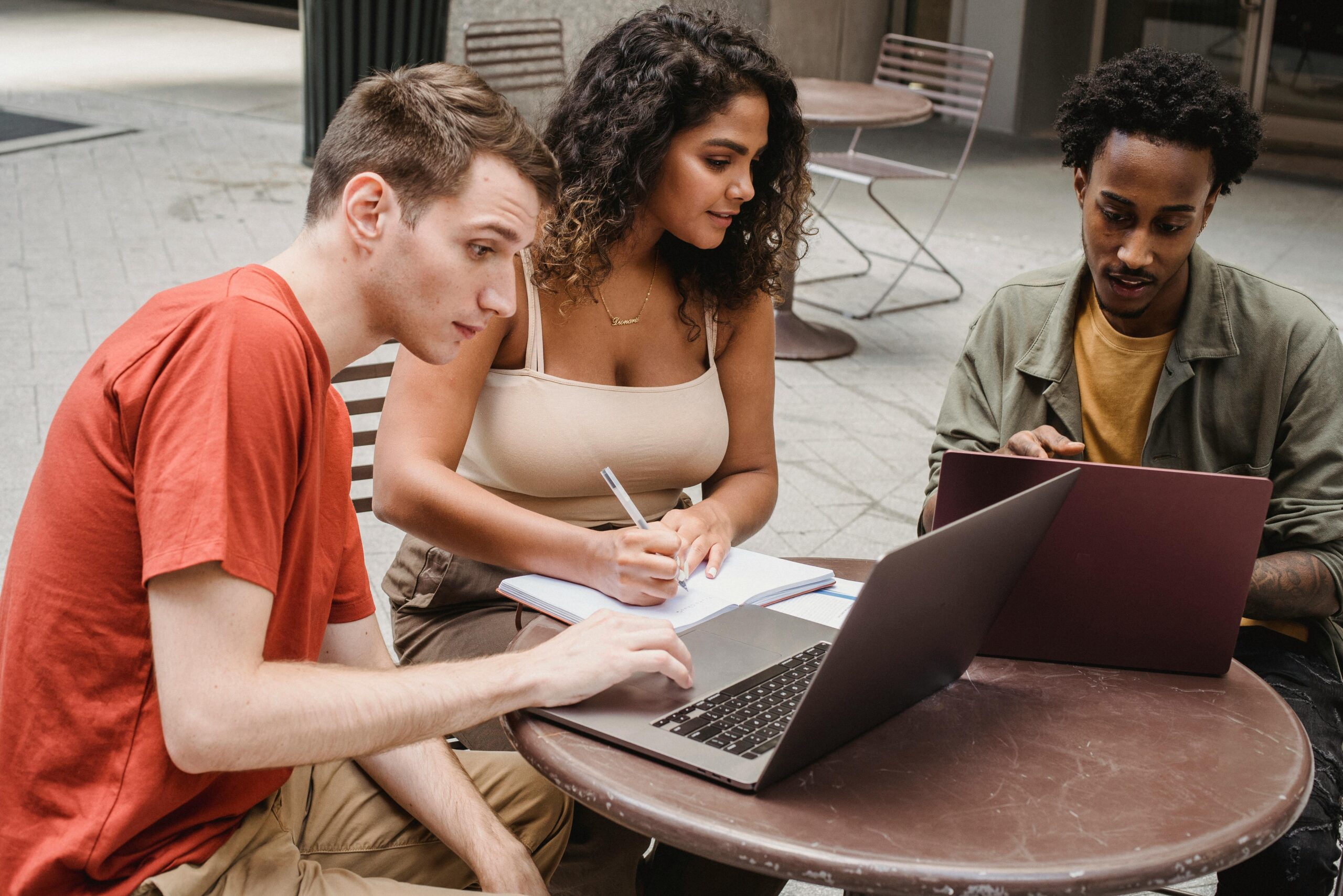 Three people collaborating at outdoor table.