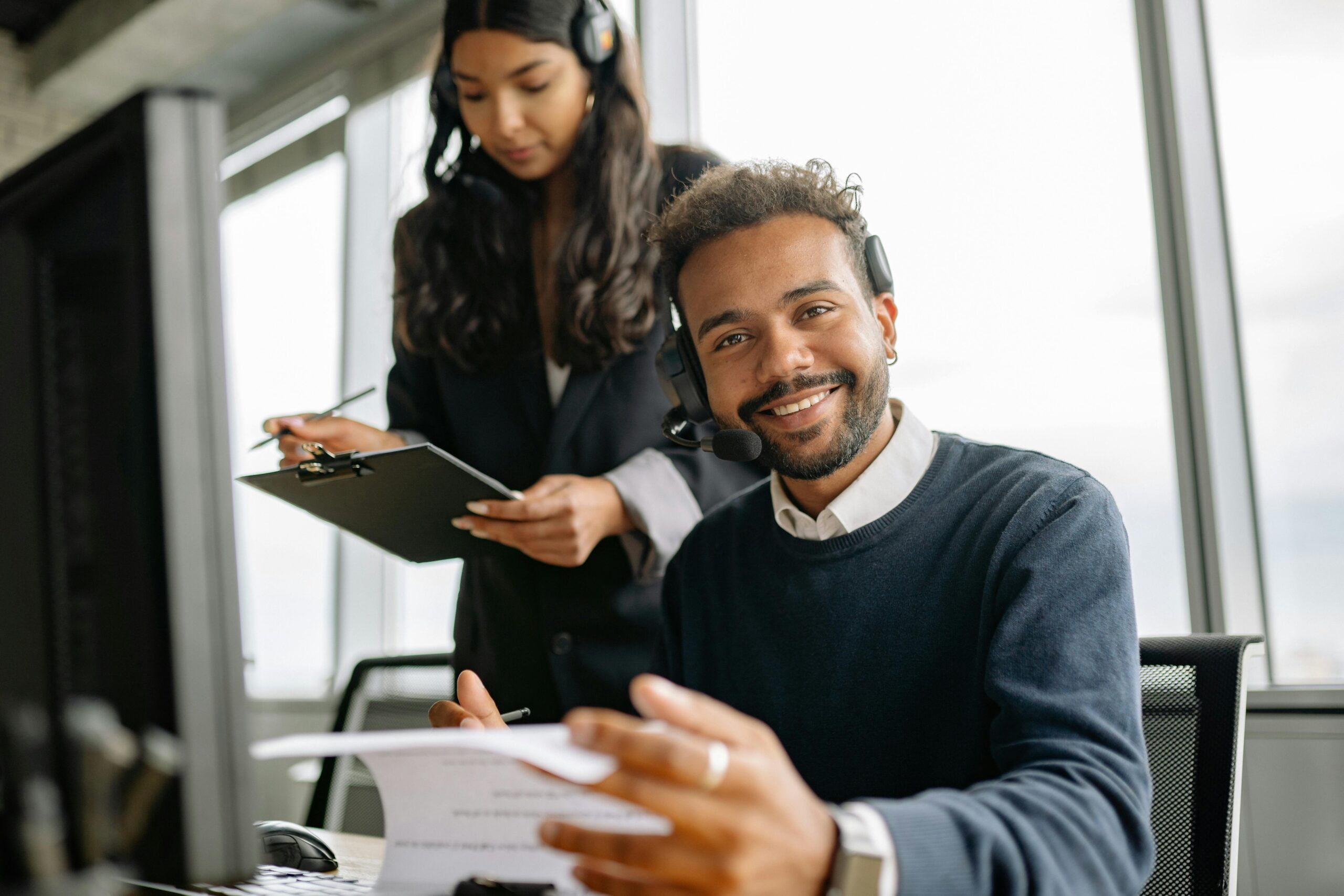 Smiling man at desk, woman with clipboard.